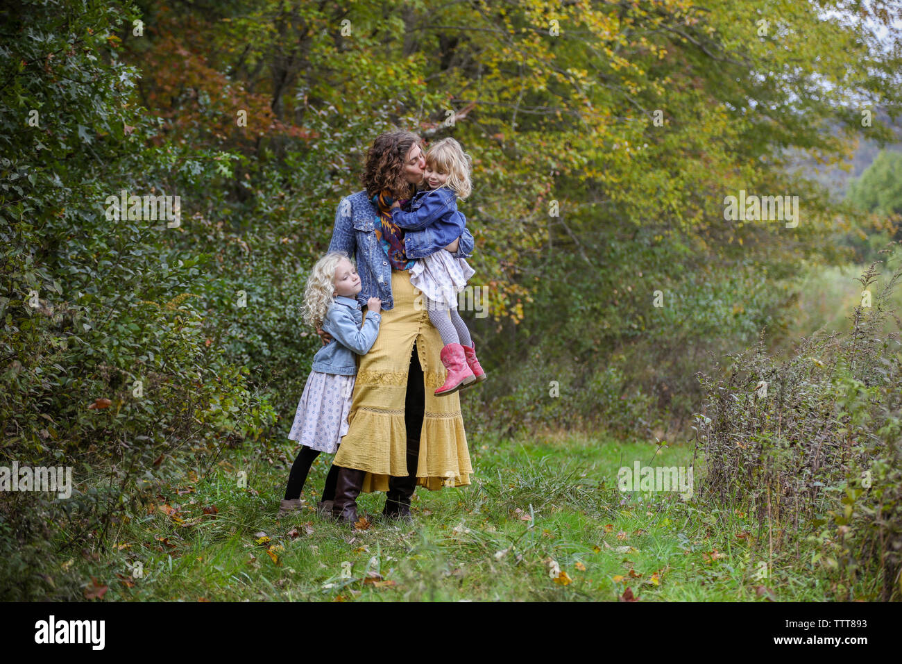 Madre di due bambini in piedi insieme baciare bambino sulla guancia Foto Stock