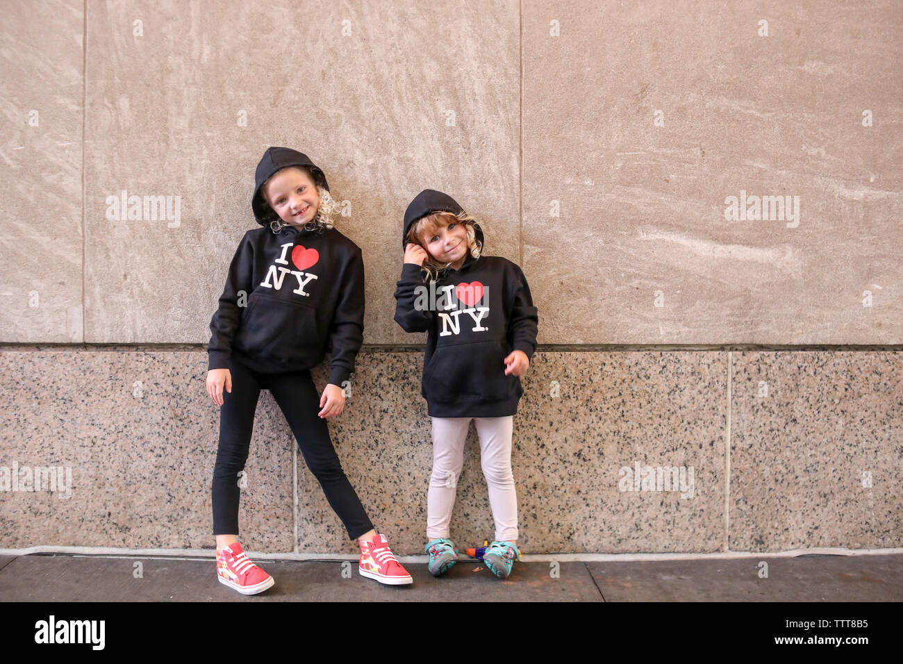 Sorelle in piedi ancora parete corrispondente indossa felpe a NYC Foto Stock