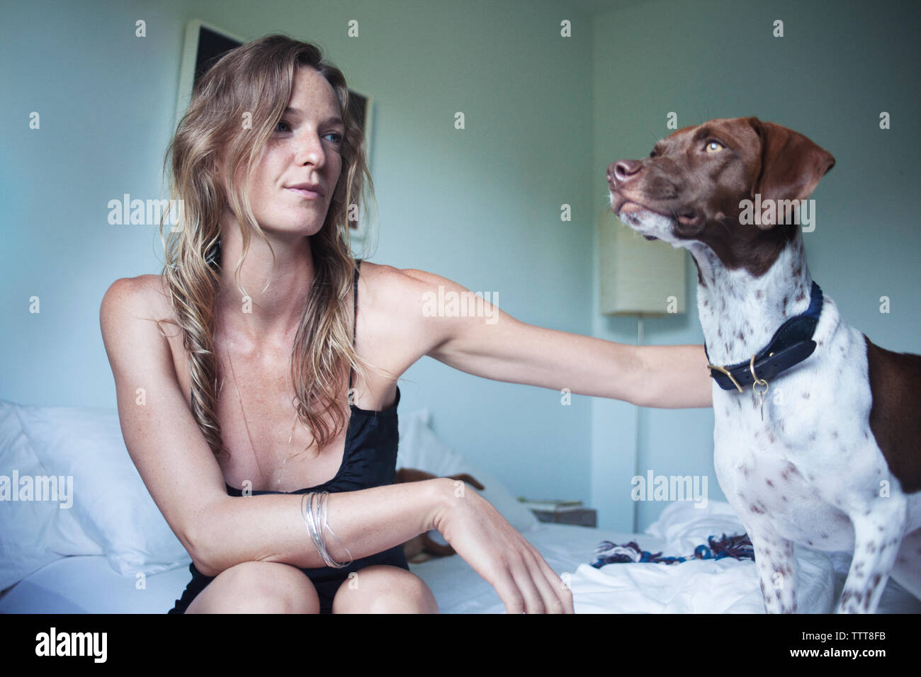 Donna sorridente con il cane seduto sul letto di casa Foto Stock