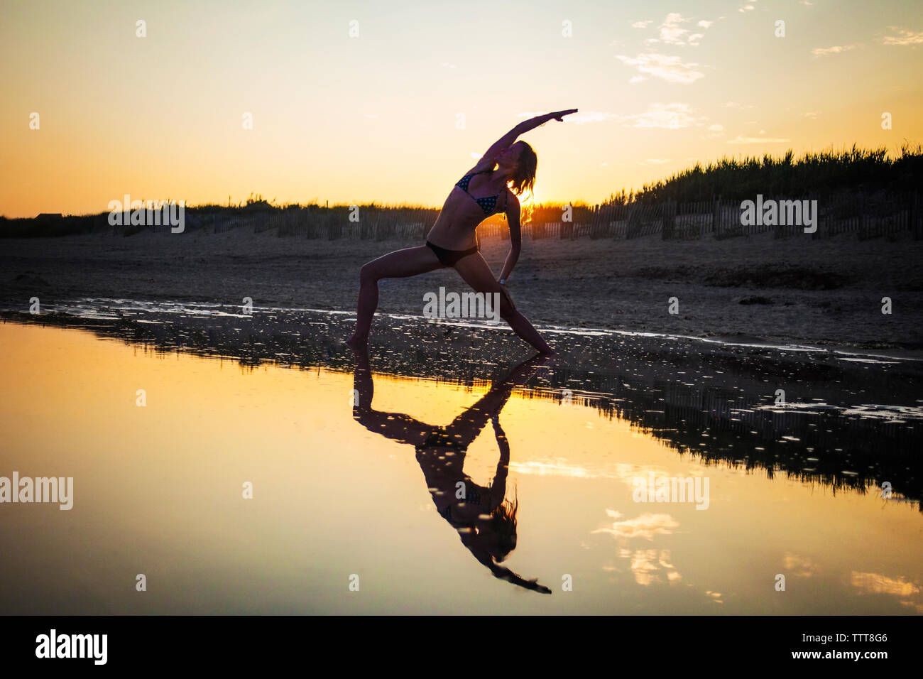 Donna che indossa un bikini a praticare yoga in spiaggia durante il tramonto Foto Stock