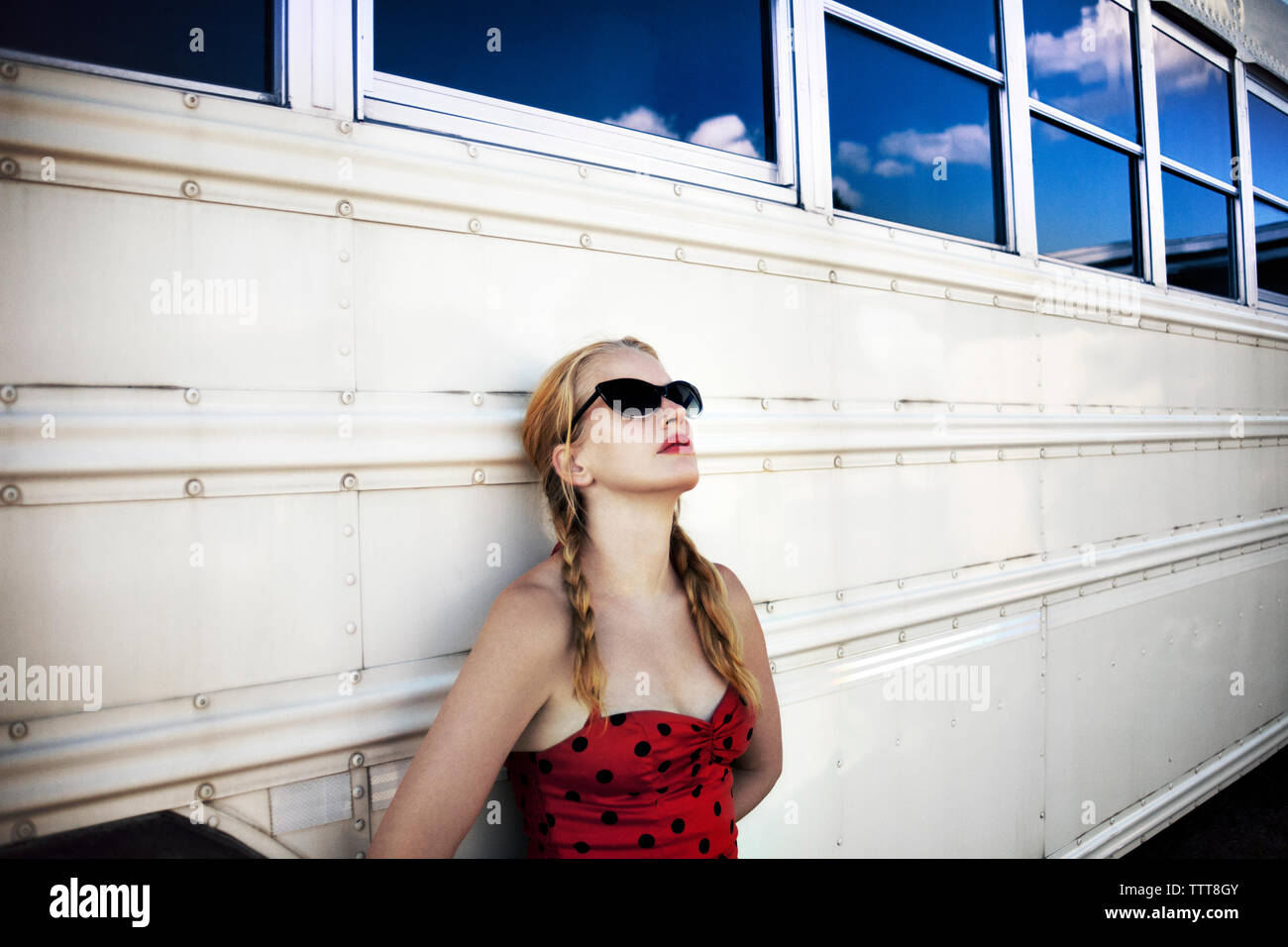 Donna che indossa gli occhiali da sole appoggiata sul bus bianco Foto Stock