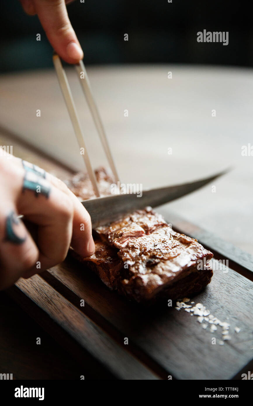 Immagine ritagliata di mani il taglio di carne arrosto su tavola Foto Stock
