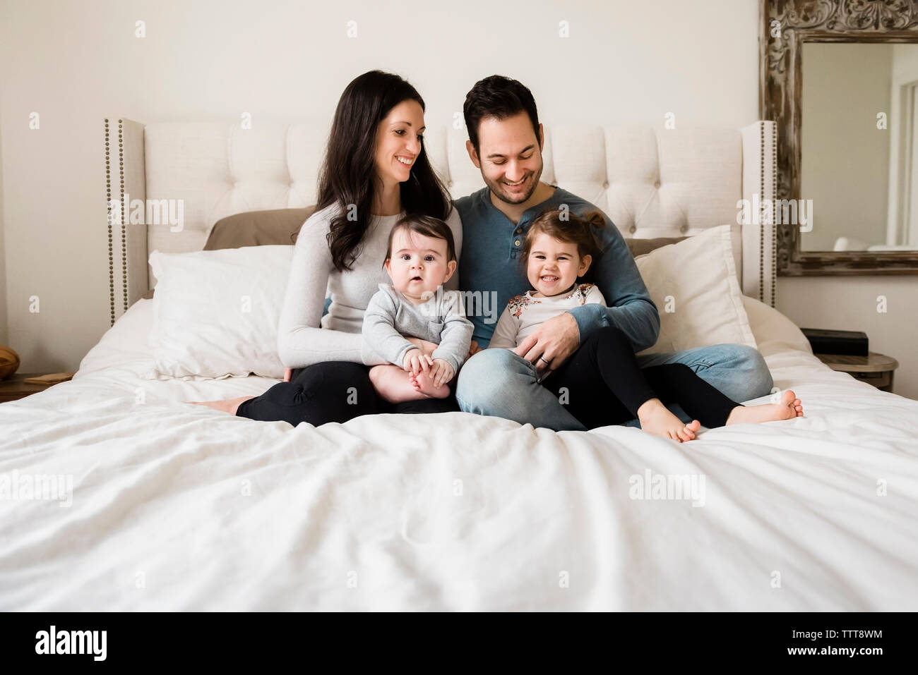 La famiglia felice seduta sul letto di casa Foto Stock