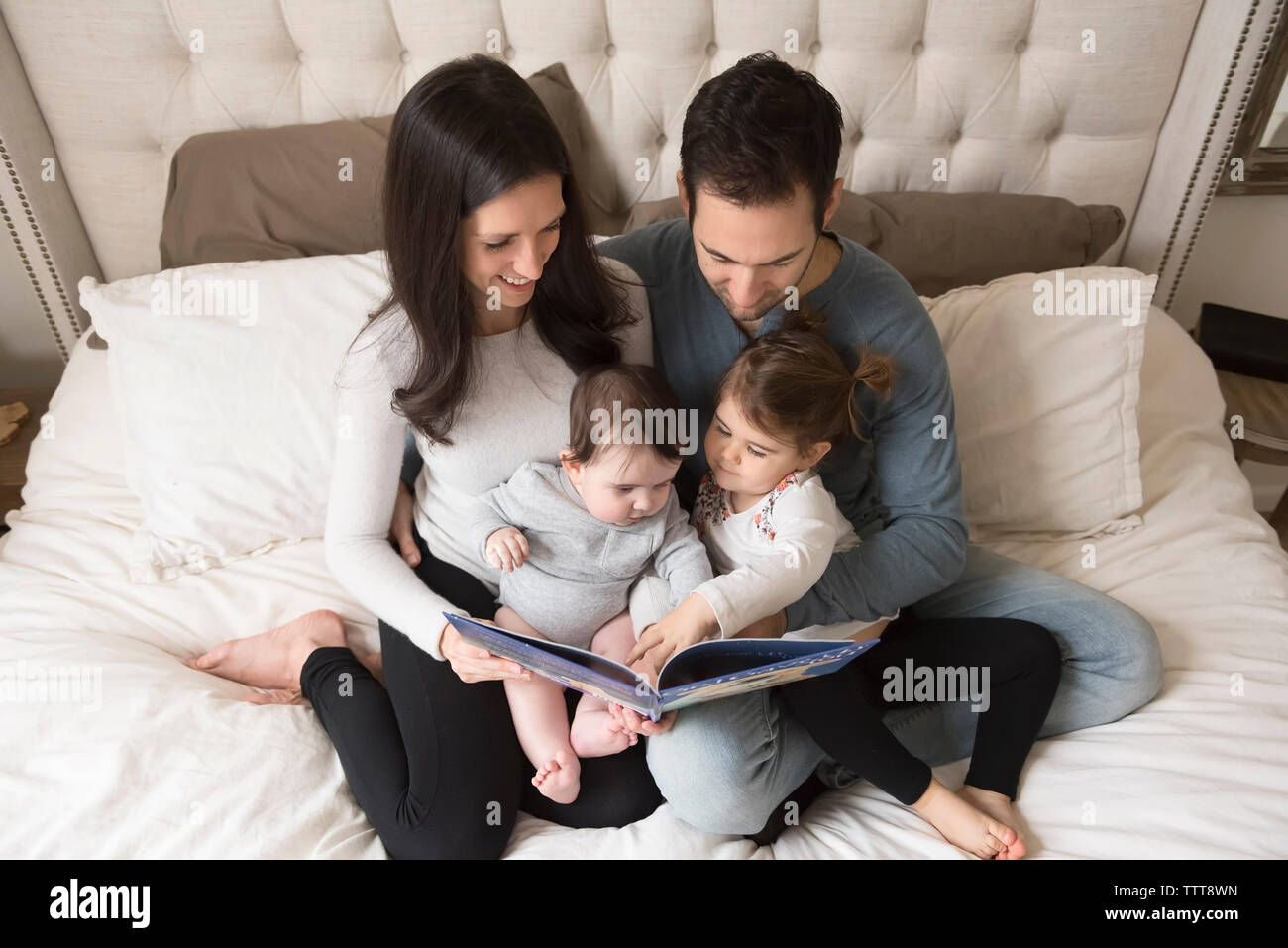 Elevato angolo di visione dei genitori con bambini guardando picture book seduti sul letto Foto Stock