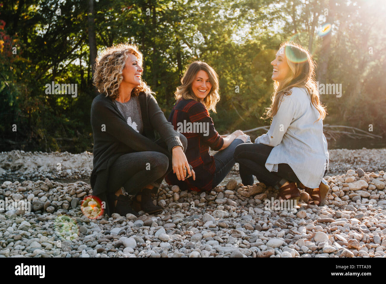 Happy amici di sesso femminile seduto su ciottoli durante la giornata di sole Foto Stock