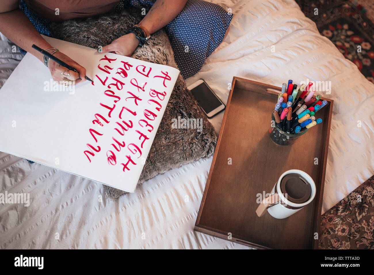 Elevato angolo di visione dell'artista Fare calligrafia mentre è seduto sul letto di casa Foto Stock