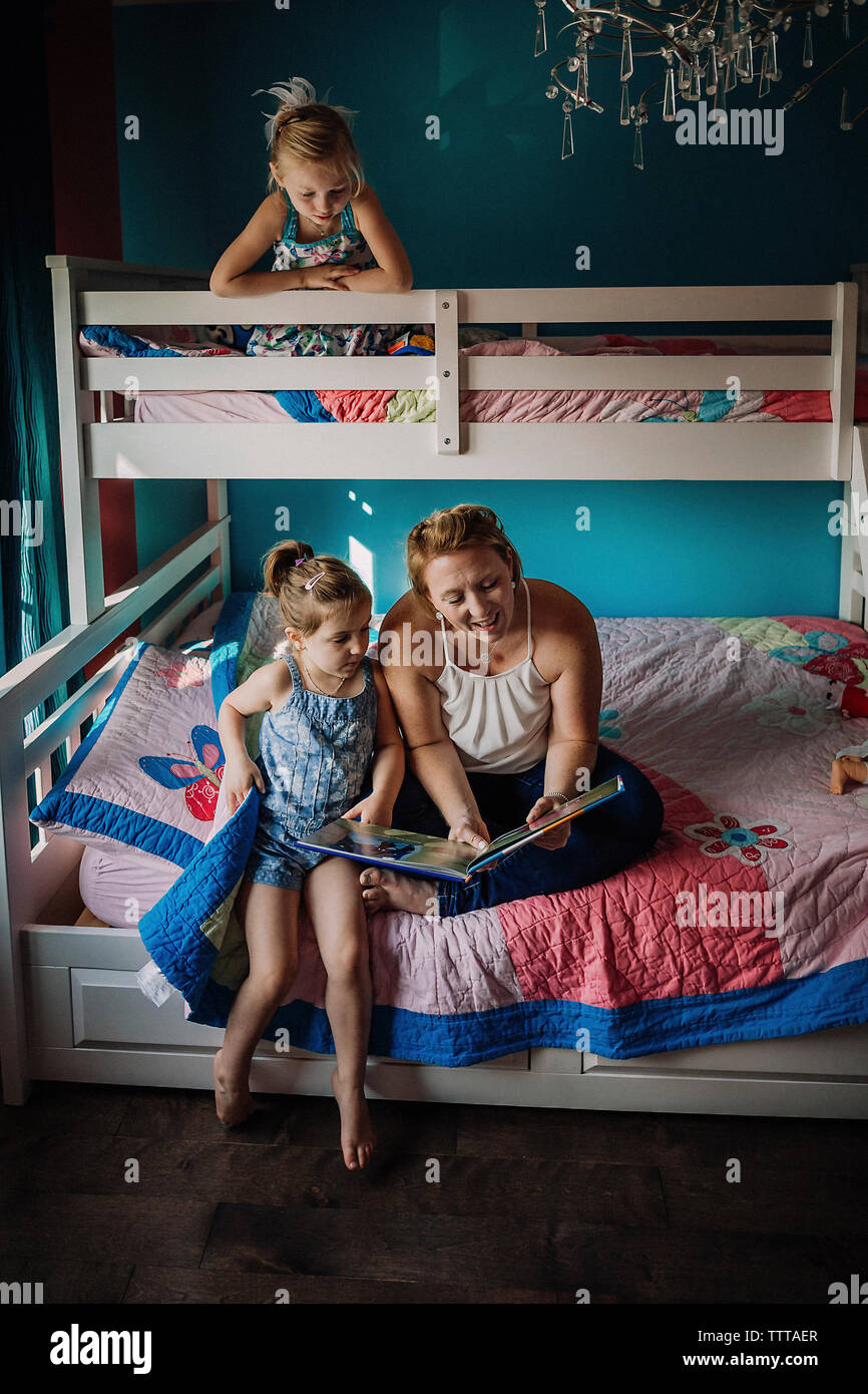 Madre libro lettura mentre è seduto con le figlie sul letto a castello a casa Foto Stock