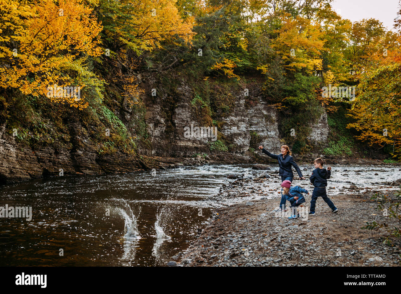 Nonna e nipoti lanciando rocce presso il fiume in autunno Foto Stock