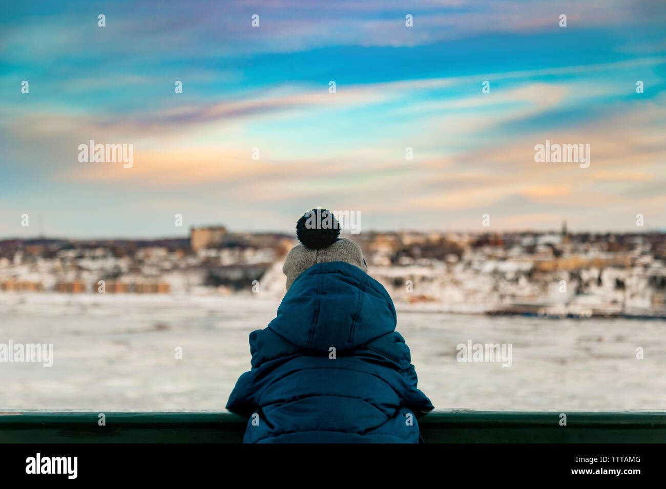 6 anni vecchio ragazzo in inverno abiti e guardare il tramonto sopra il fiume Foto Stock