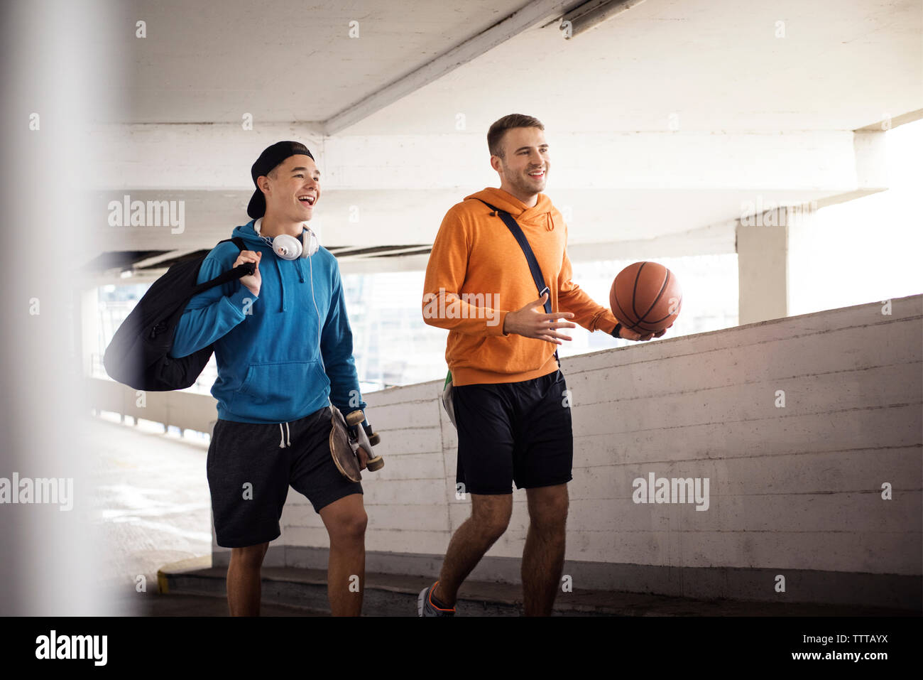 Allegro amici maschi tenendo la pallacanestro e lo skateboard mentre si cammina in parcheggio Foto Stock