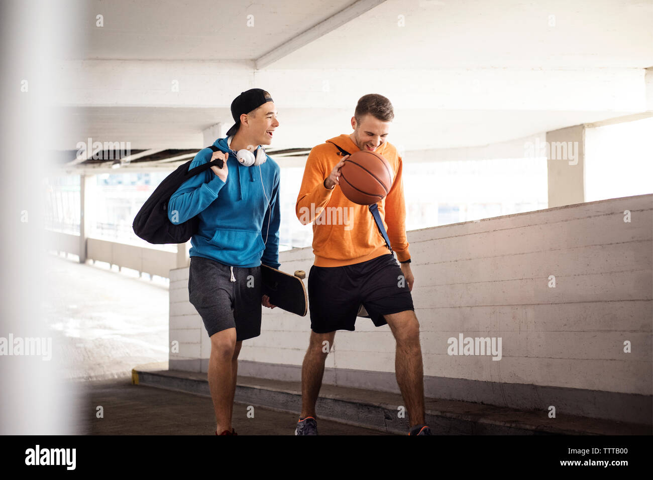 Happy amici maschi tenendo la pallacanestro e lo skateboard mentre si cammina in parcheggio Foto Stock