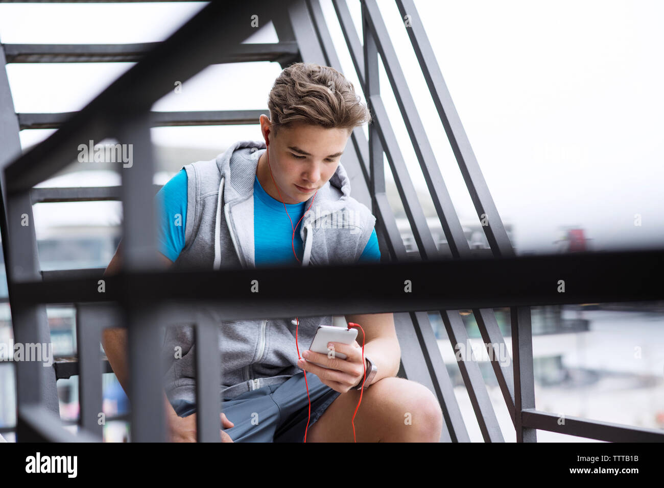 Atleta maschio utilizzando smart phone su fasi metalliche Foto Stock