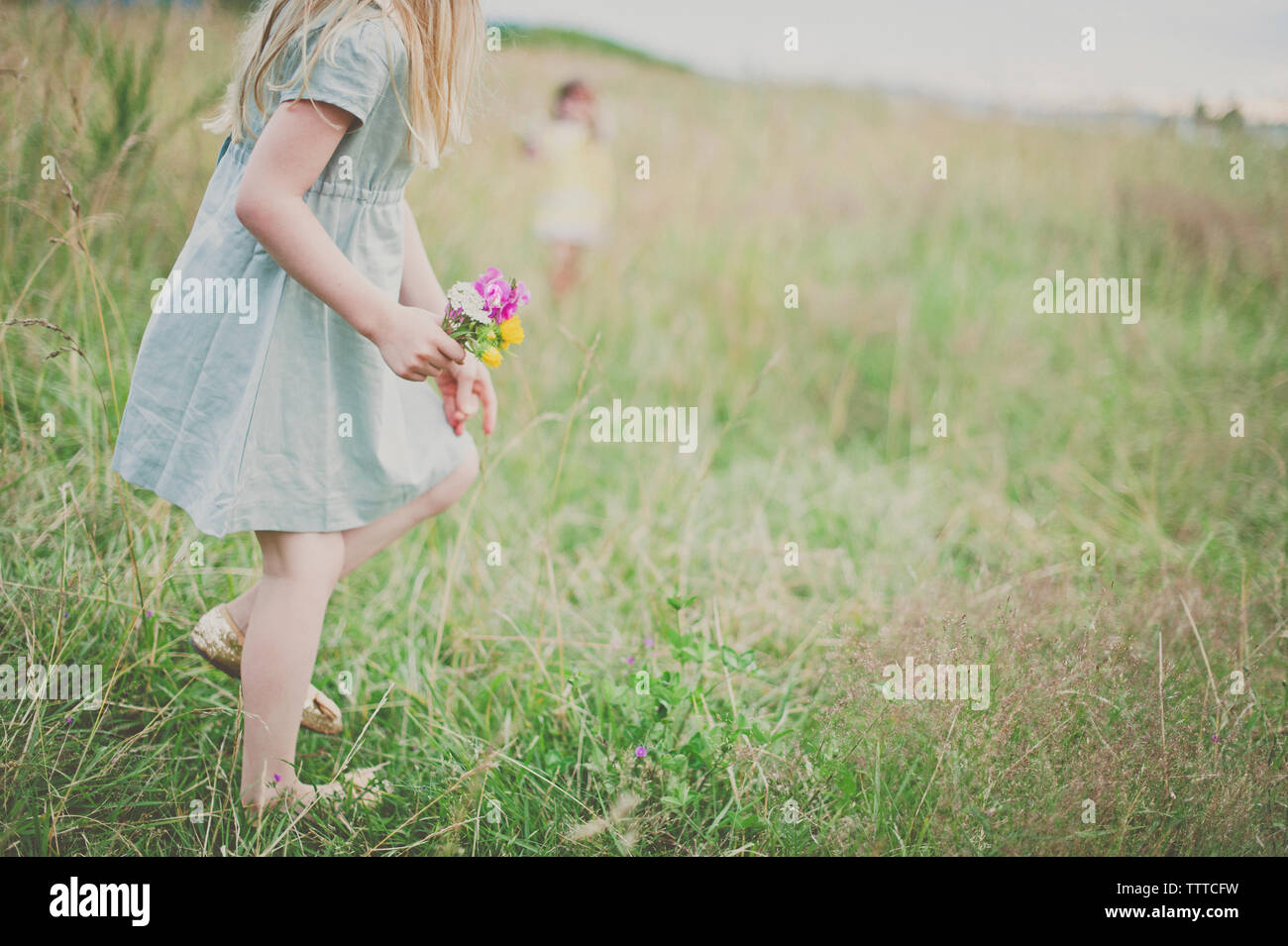 Vista laterale della ragazza con fiori sul campo con la sorella in background Foto Stock