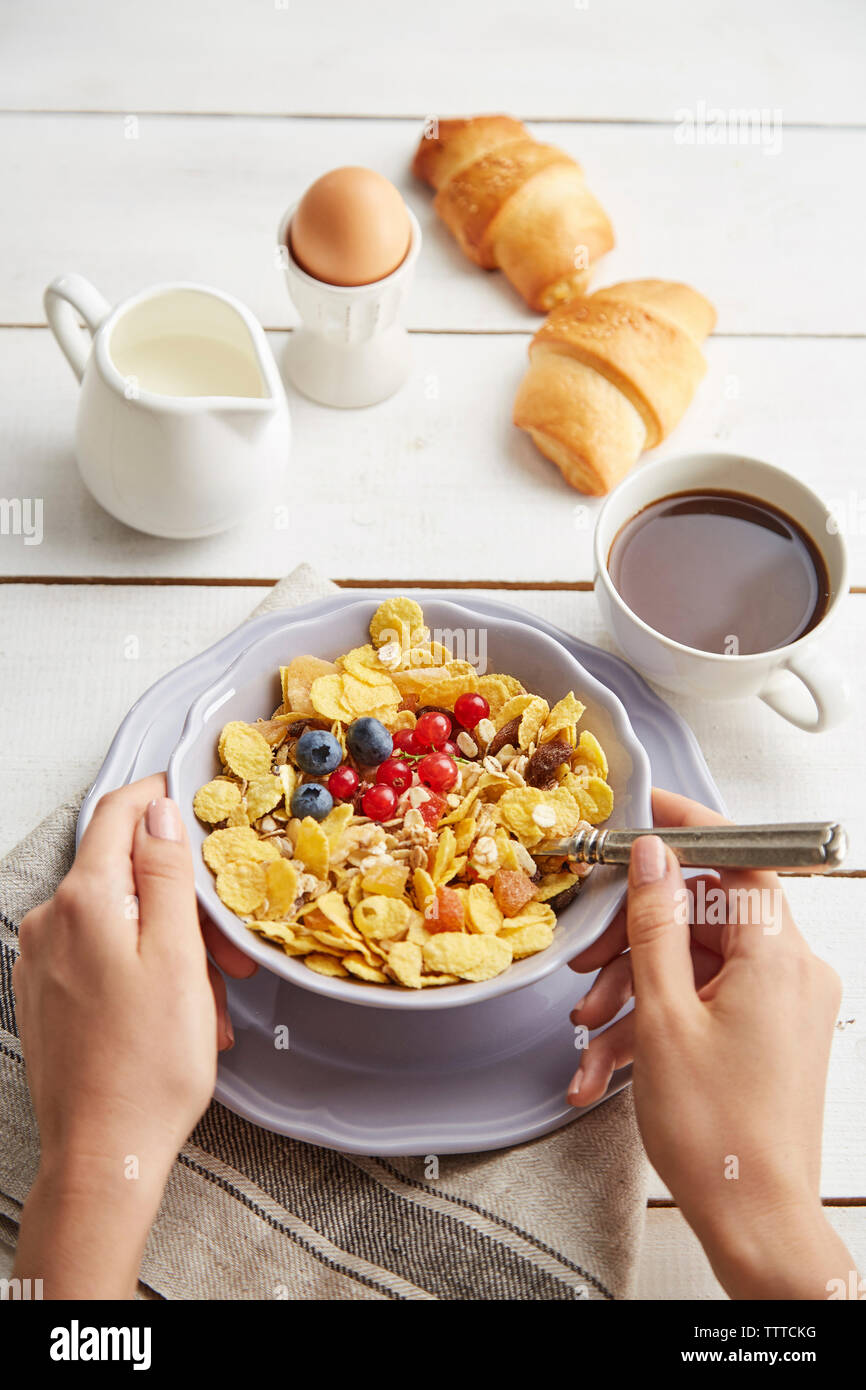 Tagliate le mani della donna tenendo la coppa con i cereali per la colazione sul tavolo a casa Foto Stock