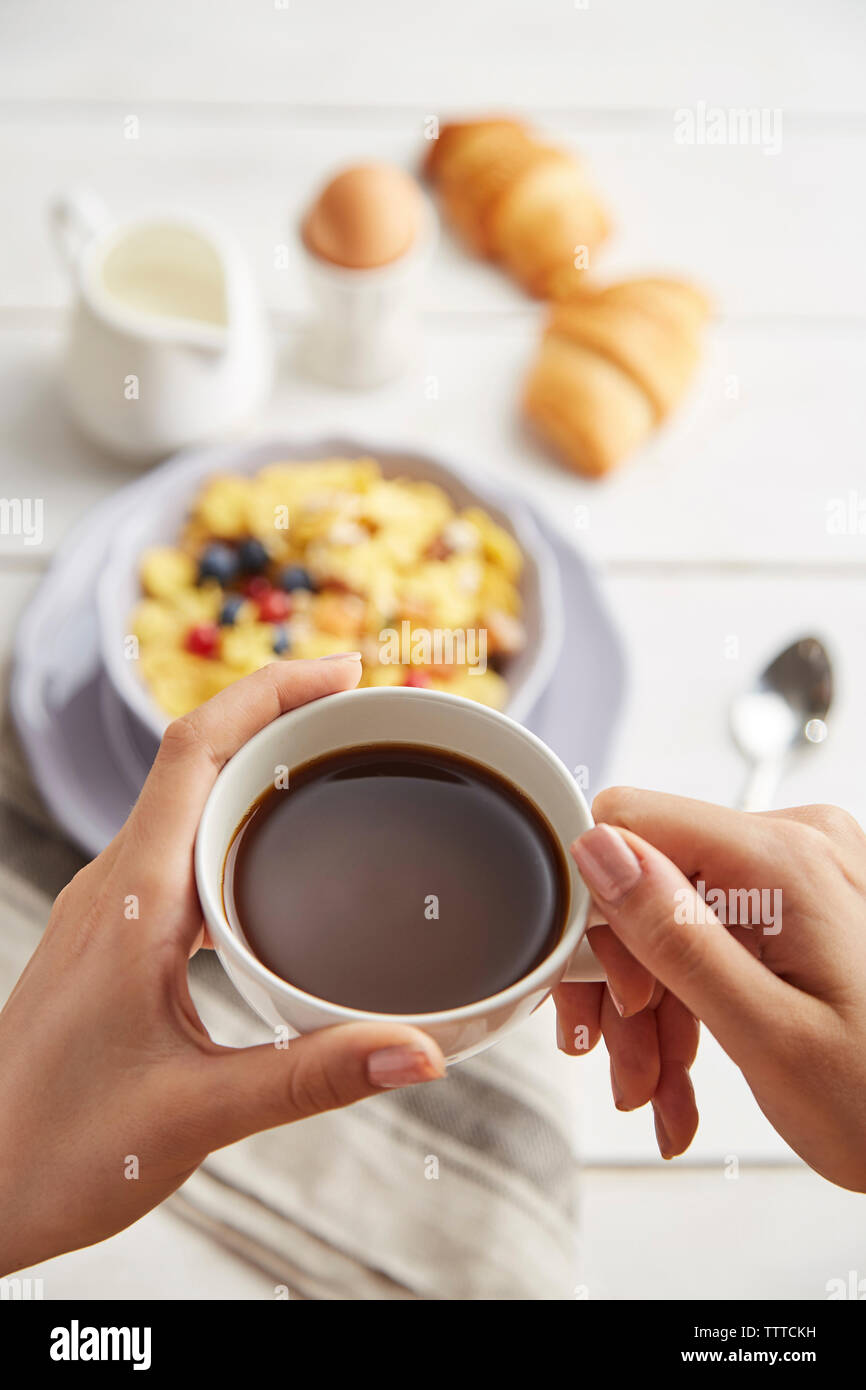 Tagliate le mani della donna azienda tazza di caffè sopra il tavolo a casa Foto Stock