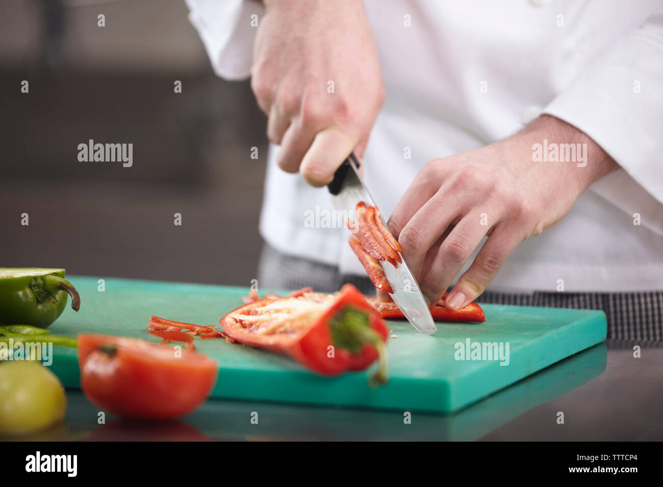 Sezione mediana dello chef la trinciatura rosso peperoncino jalapeno sul tagliere in cucina commerciale Foto Stock