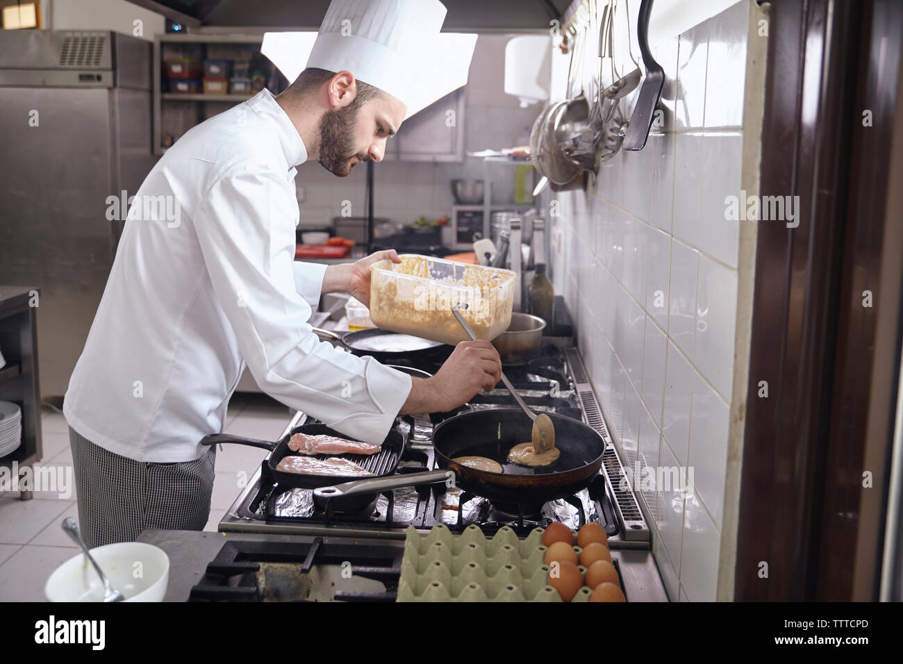 Vista laterale dello chef pancake di cottura in padella su stufa a cucina commerciale Foto Stock