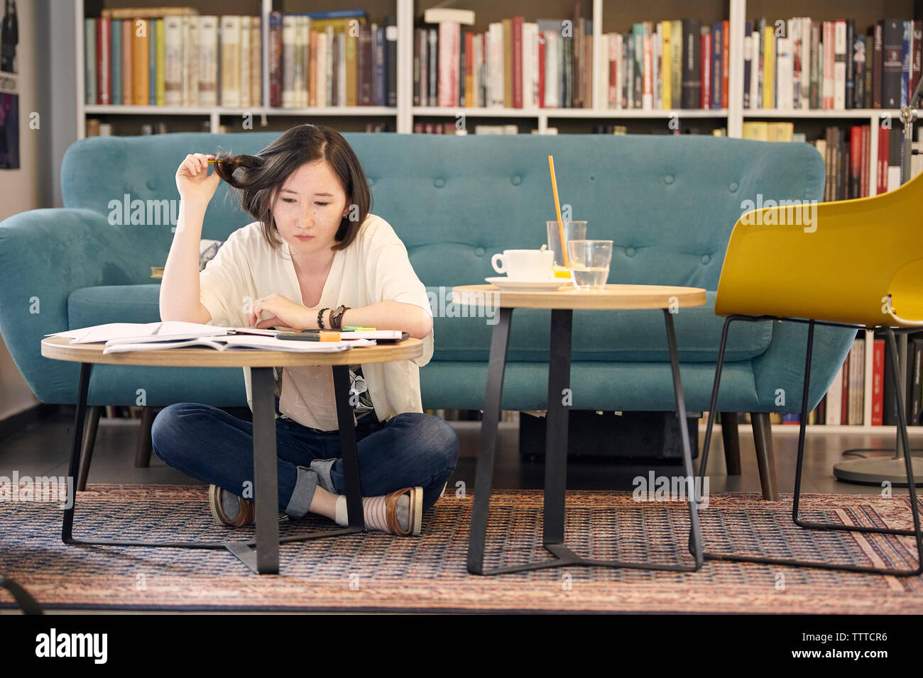 Per tutta la lunghezza della giovane donna studiare seduti dal divano su un tappeto a casa Foto Stock