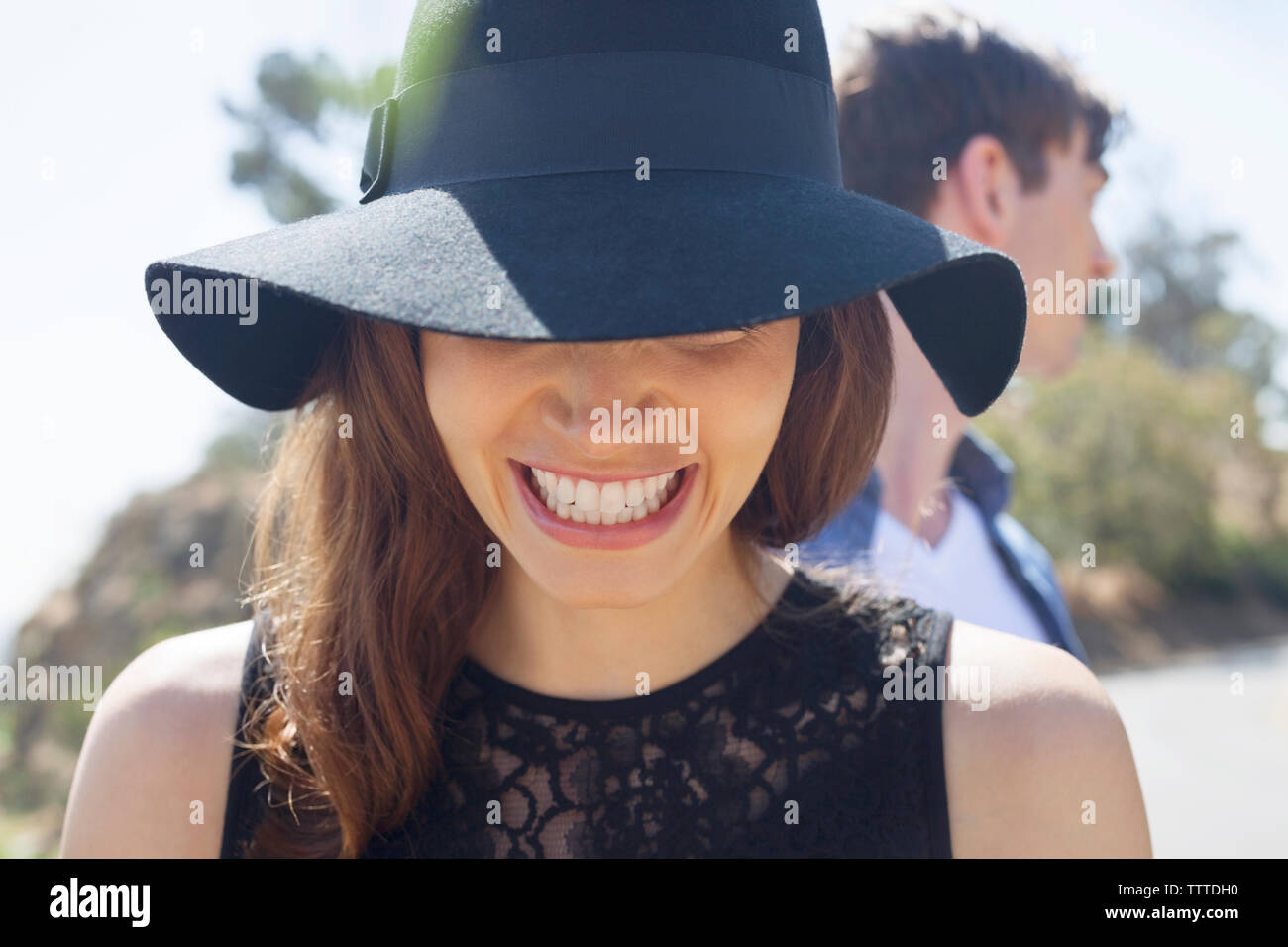Close-up di felice donna vestita di nero con cappello di amico maschio in background Foto Stock