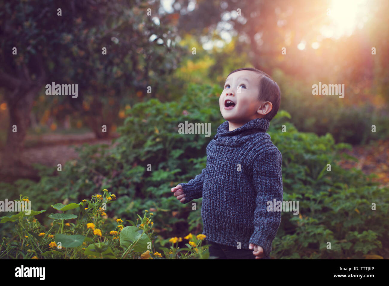 Carino giocoso baby boy con la bocca aperta permanente contro piante in posizione di parcheggio Foto Stock