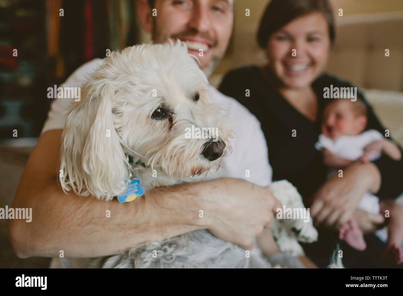 Sorridente genitori bambino portando la ragazza e il cane mentre è seduto sul letto di casa Foto Stock