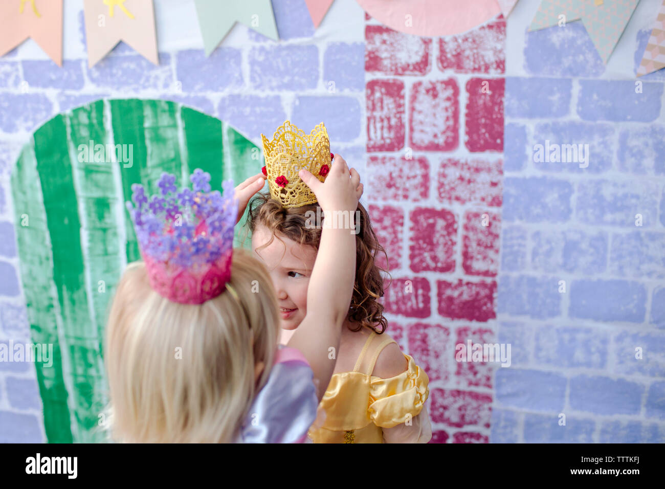 Angolo di Alta Vista della ragazza che indossa la corona ad un amico mentre in piedi contro il castello durante la principessa party Foto Stock