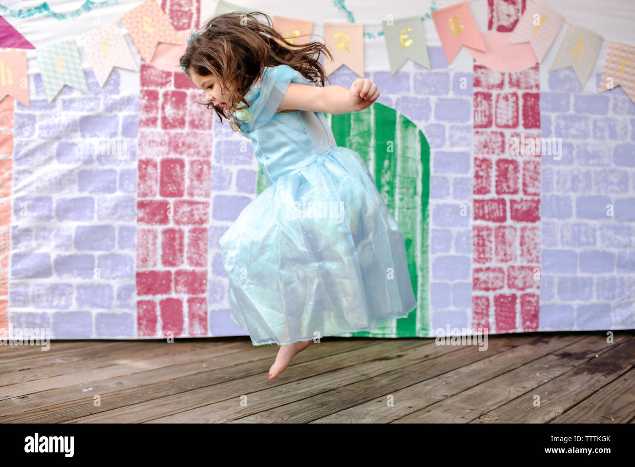 Vista laterale della ragazza di saltare sul tavolato castello contro la pittura durante la principessa party Foto Stock