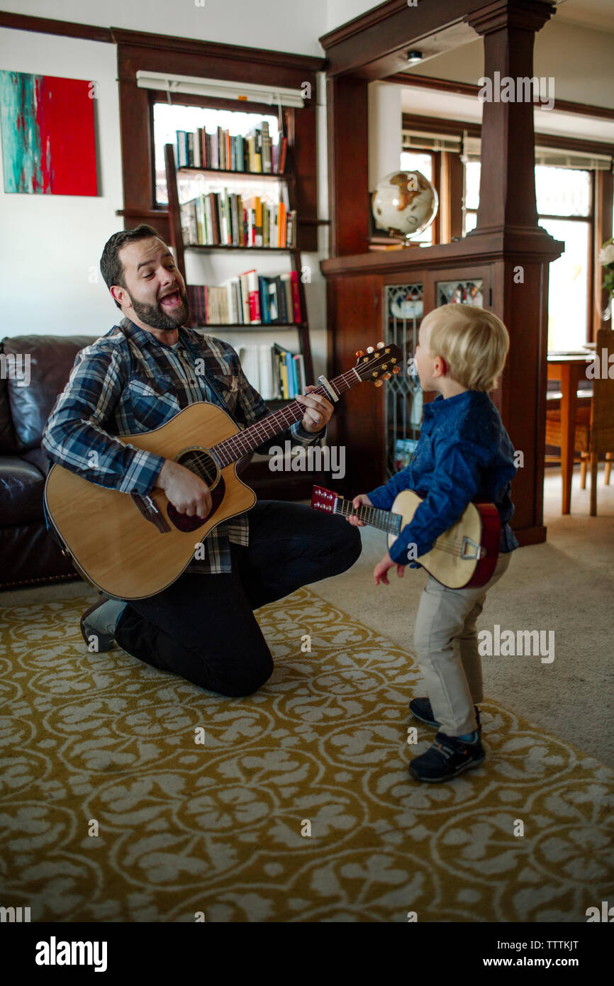 Padre con figlio cantare durante la riproduzione di chitarre a casa Foto Stock