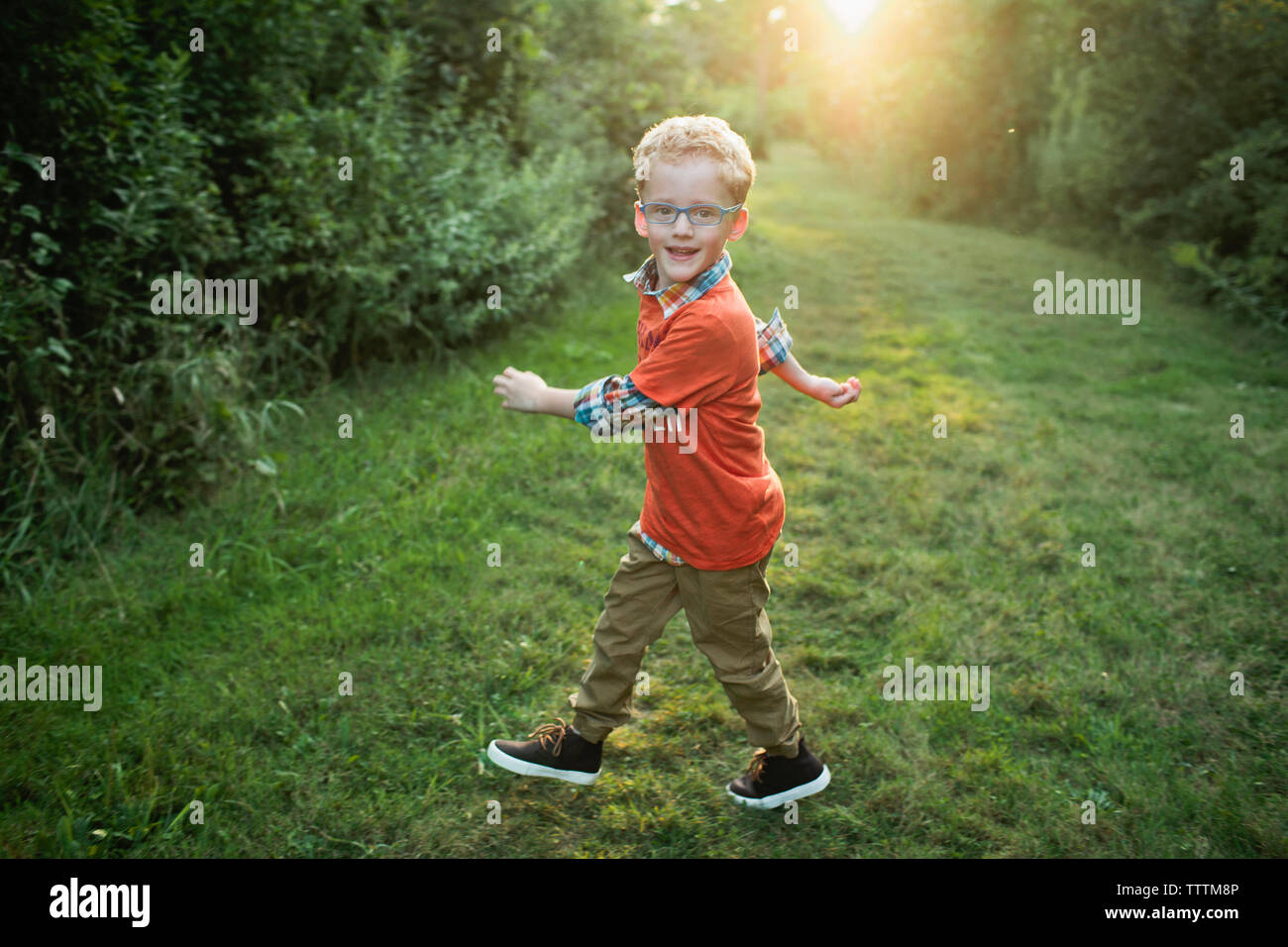 Ritratto di ragazzo sorridente camminando sul campo erboso in foresta Foto Stock
