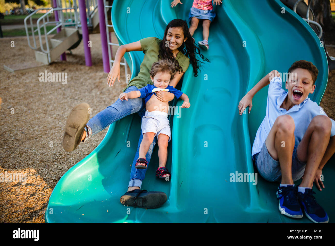 Allegro fratelli scorrevole su diapositive in un parco giochi Foto Stock