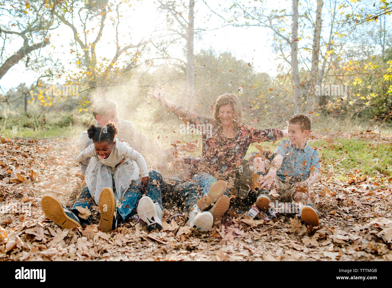 Famiglia giocando con foglie durante la seduta sul campo al parco durante l'autunno Foto Stock