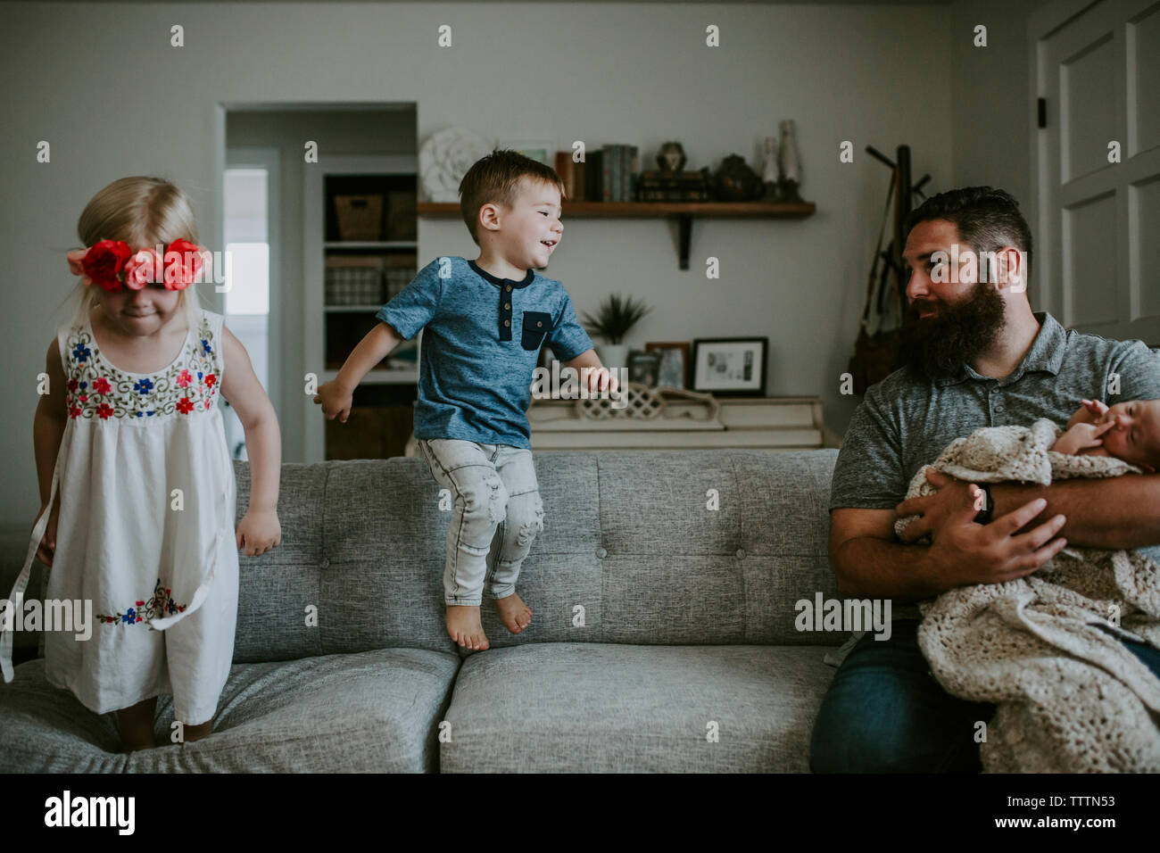 Padre che porta la figlia del neonato guardando i bambini che giocano sul divano nel soggiorno Foto Stock