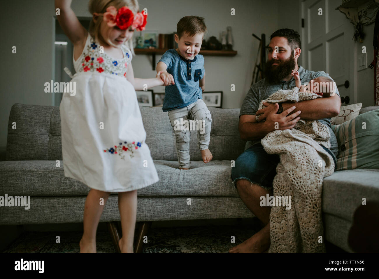 Padre che porta la figlia del neonato guardando i bambini che giocano nel soggiorno Foto Stock