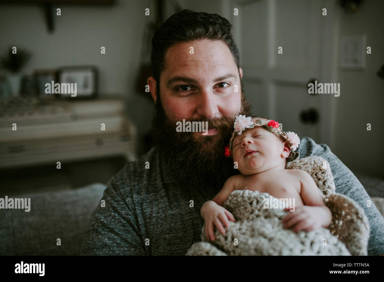 Ritratto di Padre barbuto che trasportano carino sleeping figlia indossa tiara comodamente seduti sul divano di casa Foto Stock