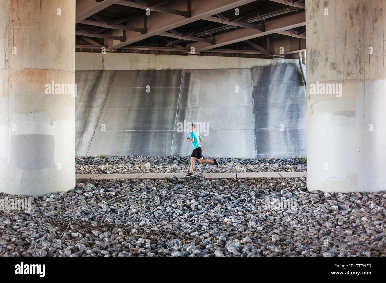 Atleta maschio jogging sulla strada sotto il ponte Foto Stock