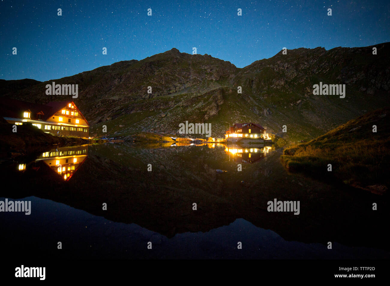 La riflessione di case illuminate nel lago di notte Foto Stock