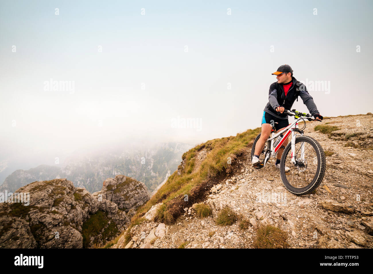 Atleta maschio con la bicicletta sul monte contro sky Foto Stock