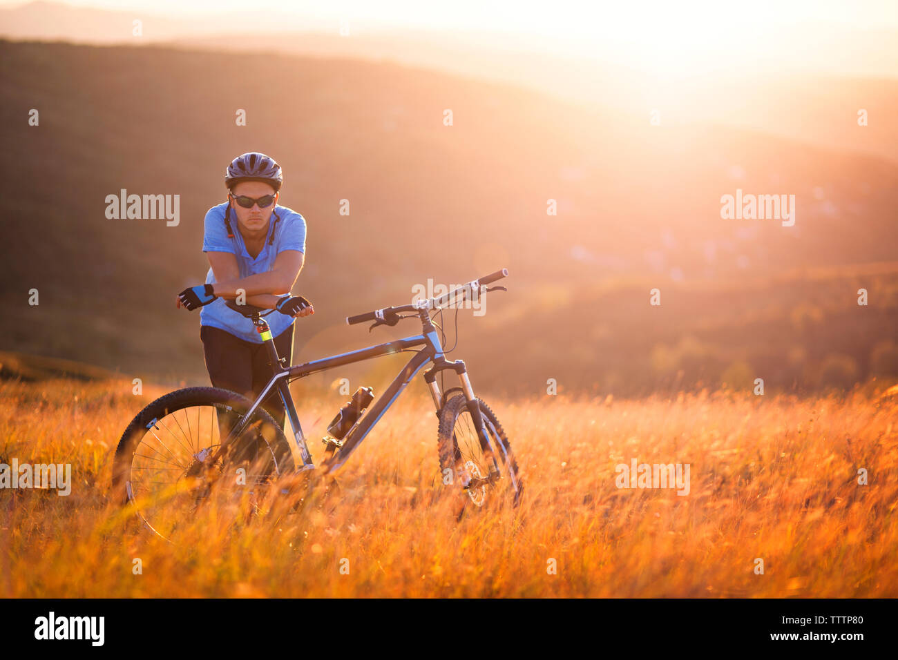 Ritratto di atleta maschio in piedi in bicicletta sul campo durante il tramonto Foto Stock