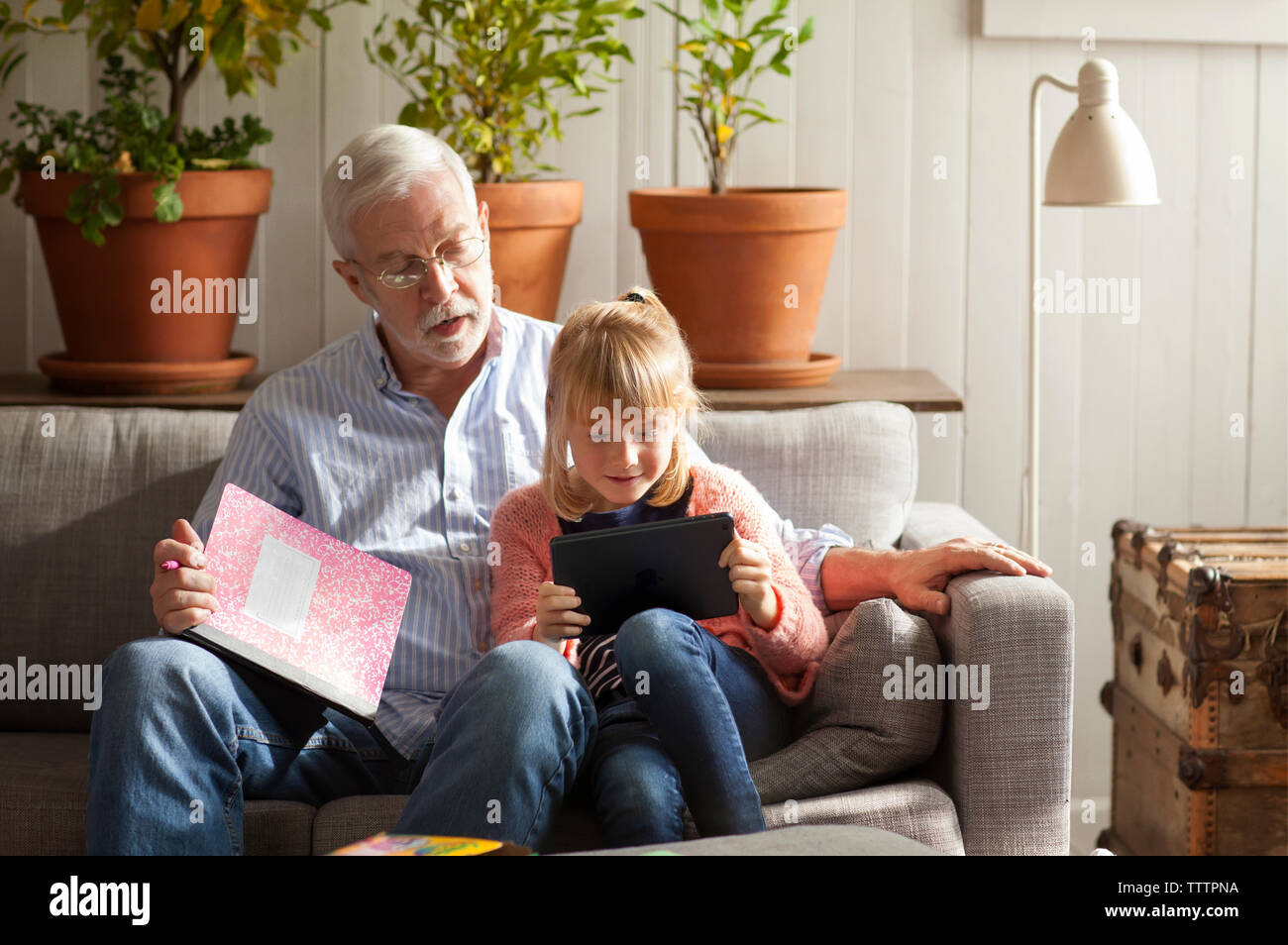Ragazza utilizzando computer tavoletta mentre è seduto con il nonno sul divano di casa Foto Stock