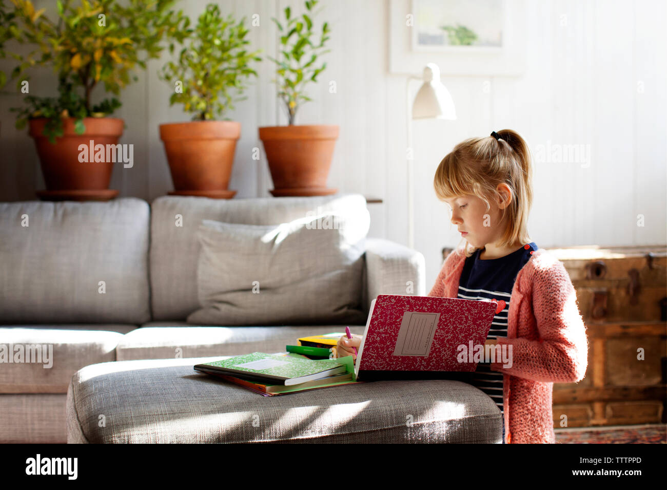 Ragazza che studiano in ginocchio dal divano di casa Foto Stock