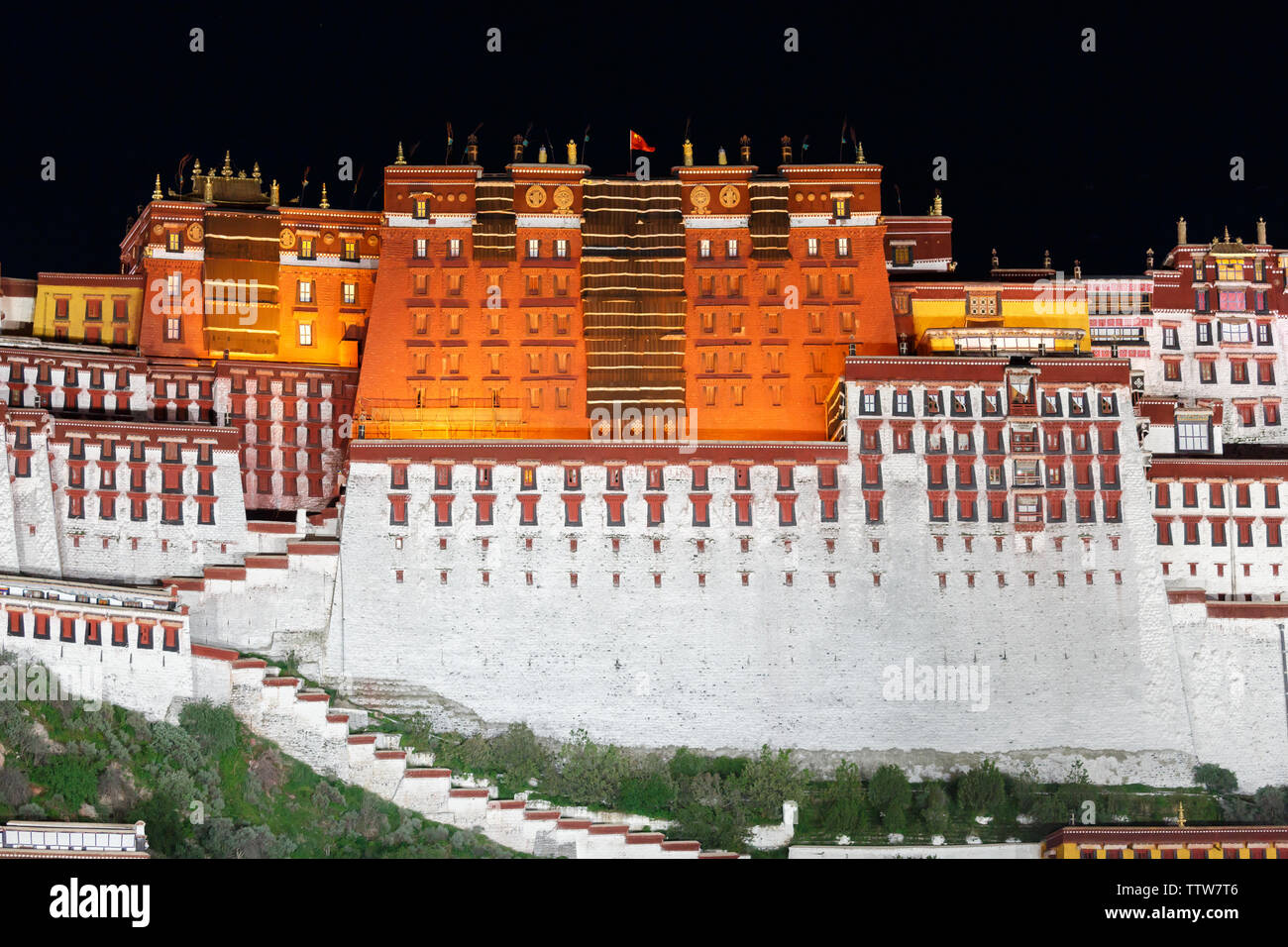 In prossimità della parte principale del palazzo del Potala di notte (Lhasa, in Tibet). Cielo nero, la bandiera cinese sventola sulla sommità del palazzo, rossa e bianca facciata illuminata. Foto Stock