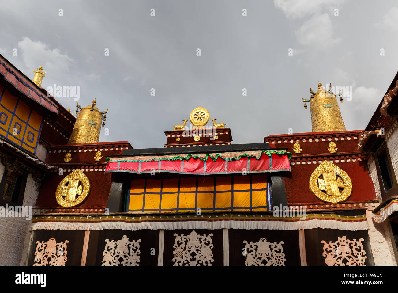 Vista sul tetto del Jokhang Tempio. Una ruota di Dharma con due cervi e ruote della preghiera corona il famoso tempio. Buddismo tibetano, ornamenti, arte buddista. Foto Stock