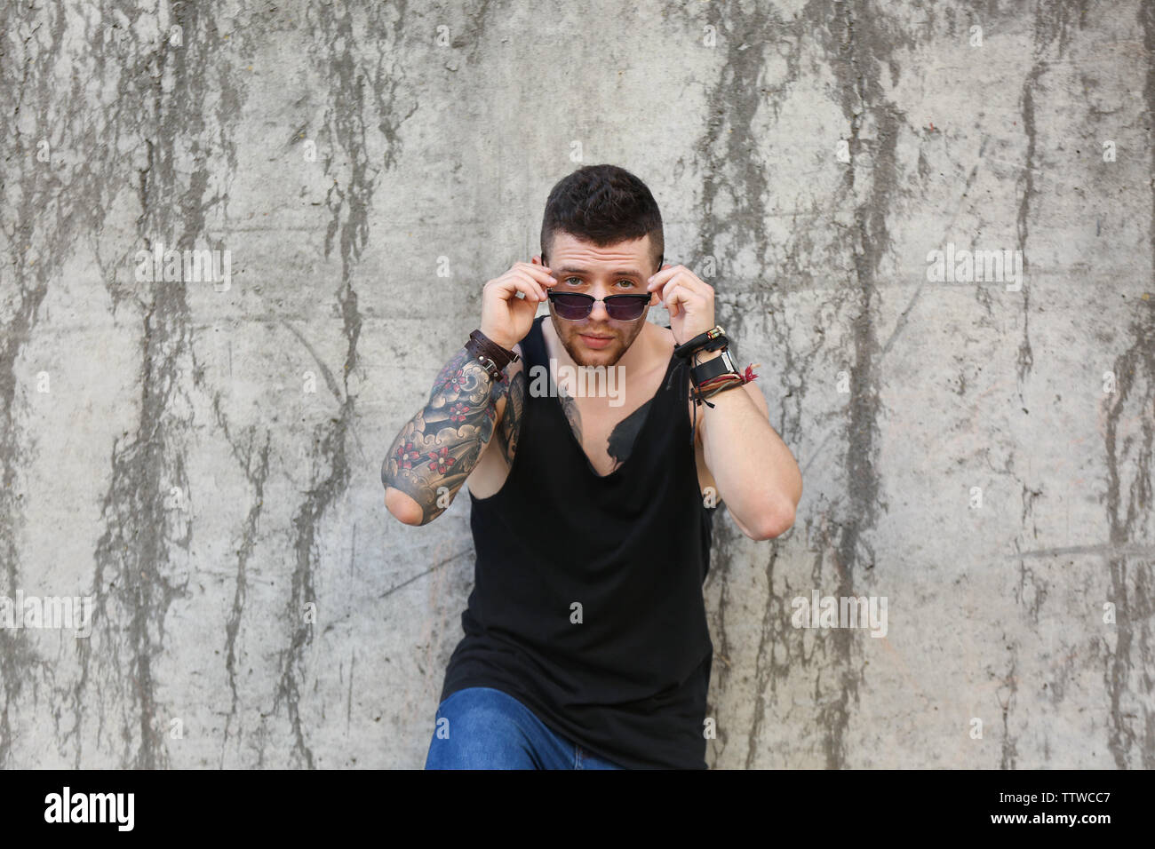 Giovane uomo tatuato in posa sul calcestruzzo sporco sullo sfondo della parete Foto Stock