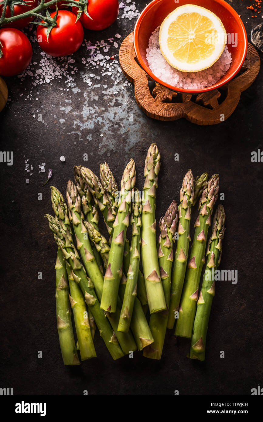 Asparagi freschi mazzetto on dark rustico tavolo da cucina con ingredienti, vista dall'alto. Mangiare sano e cucina stagionale Foto Stock