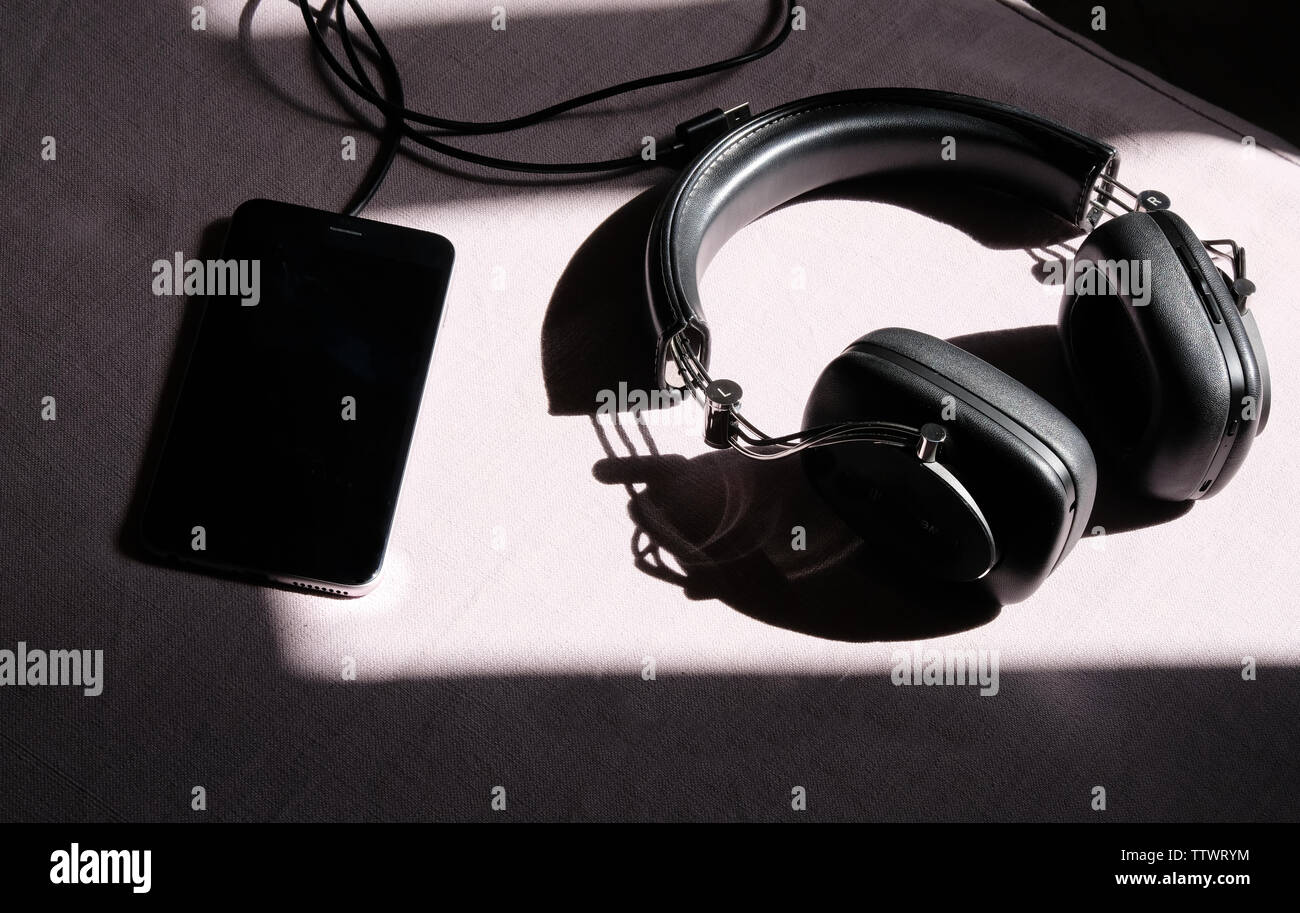 Le cuffie e lo smartphone sdraiati al sole su un tavolo bianco Foto Stock
