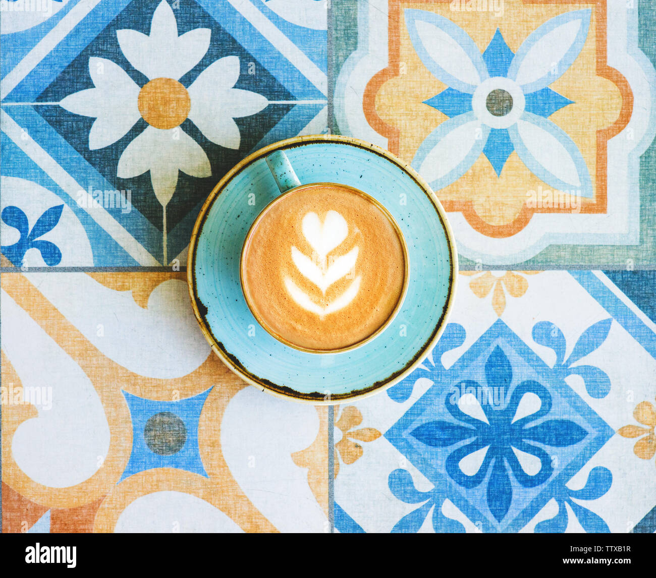 Caffè con latte art in blu sulla tazza colorata Sfondo piastrelle. Vista dall'alto. Foto Stock