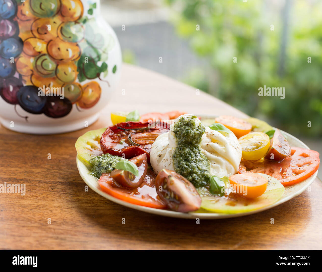 Fresh multi colorata insalata di pomodoro con mozzarella di bufala e il verde del basilico Pesto, su un tavolo esterno con piante in background Foto Stock