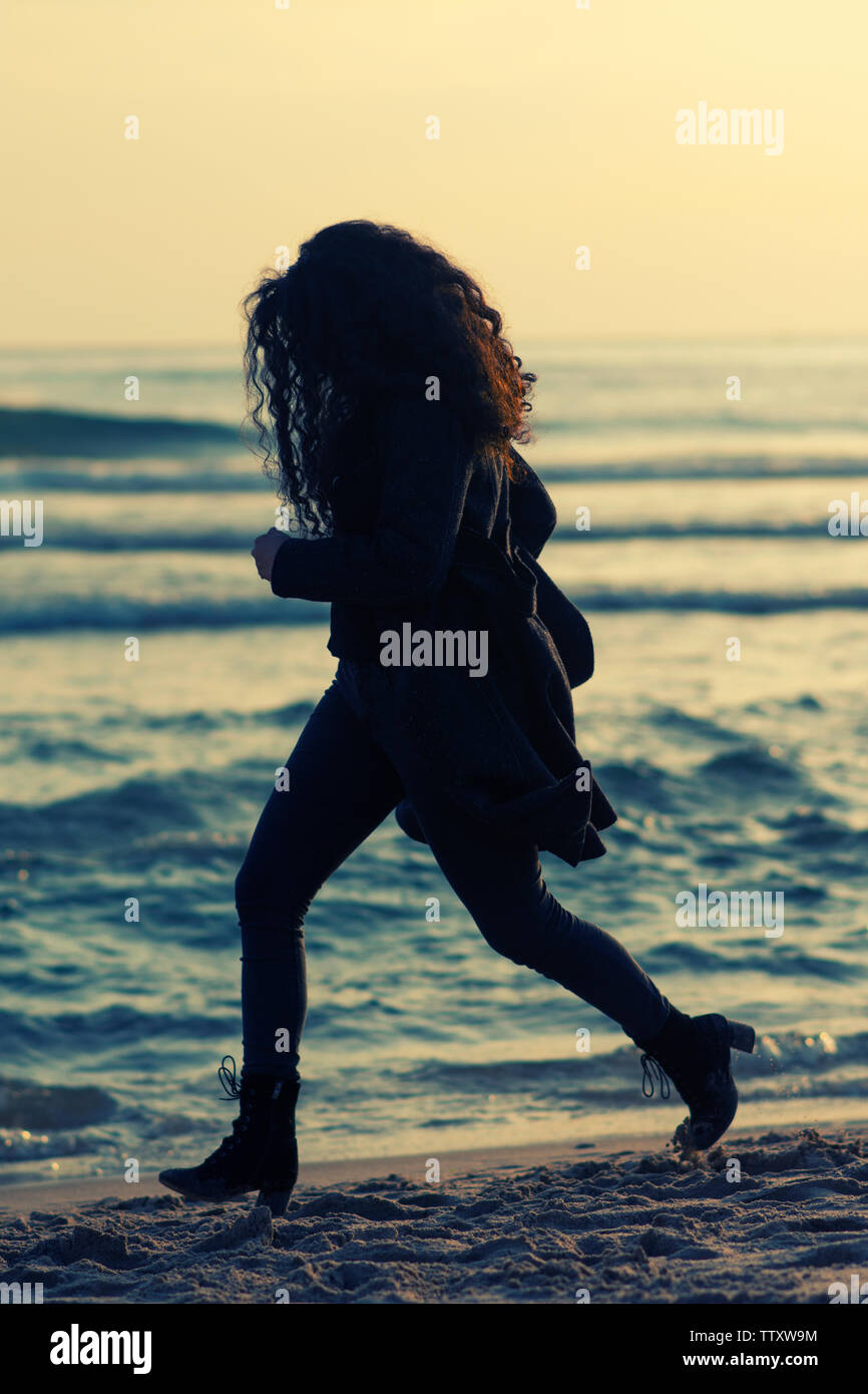 Donna che indossa rivestire in esecuzione sulla spiaggia al tramonto Foto Stock