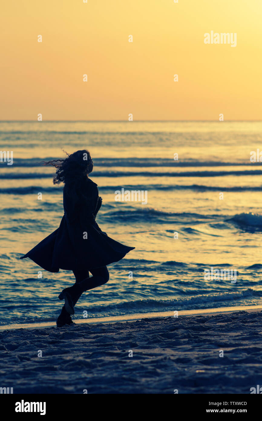 Donna che indossa rivestire in esecuzione sulla spiaggia al tramonto Foto Stock