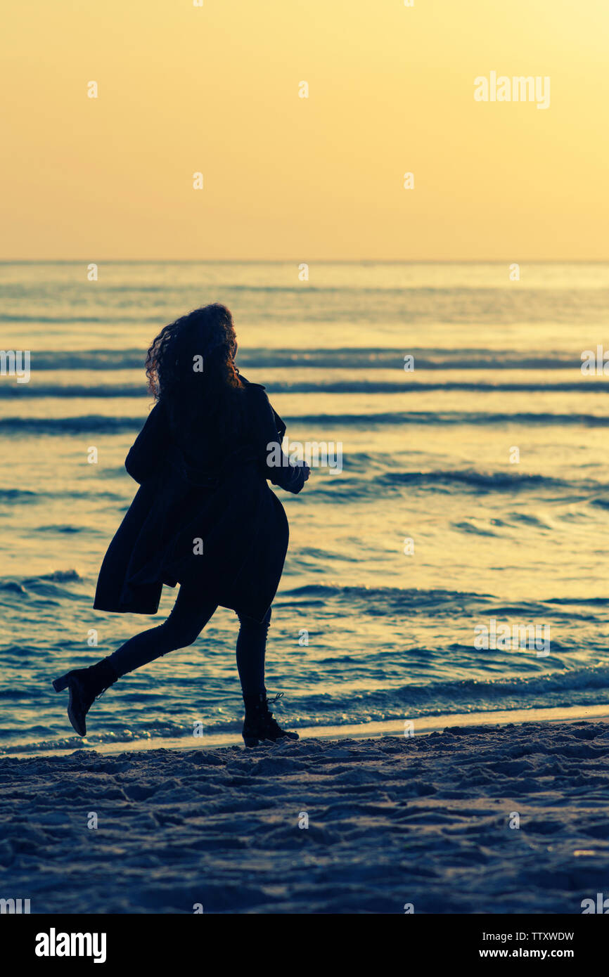 Donna che indossa rivestire in esecuzione sulla spiaggia al tramonto Foto Stock